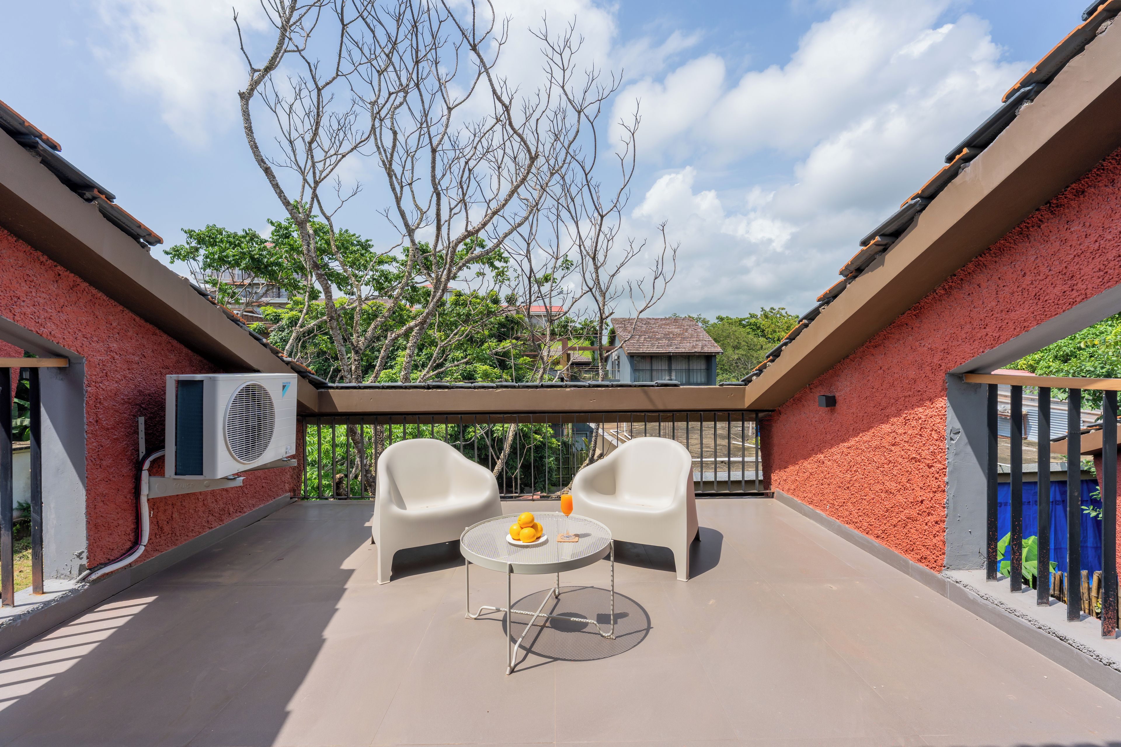A covered outdoor seating area with two chairs and a table, surrounded by a red brick wall and a glass railing.