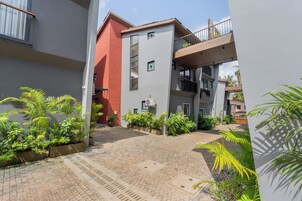 Um pátio com caminho de tijolos, plantas em vasos e um edifício com fachada vermelha e varandas.
