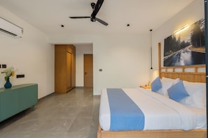 A modern bedroom with a bed, a ceiling fan, a painting, and a view of a road. - ELIVAAS Signature Coco Baia 3BHK Villa (Marra)