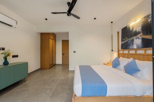 Quarto moderno com cama, ventilador de teto, pintura e vista para a rua.