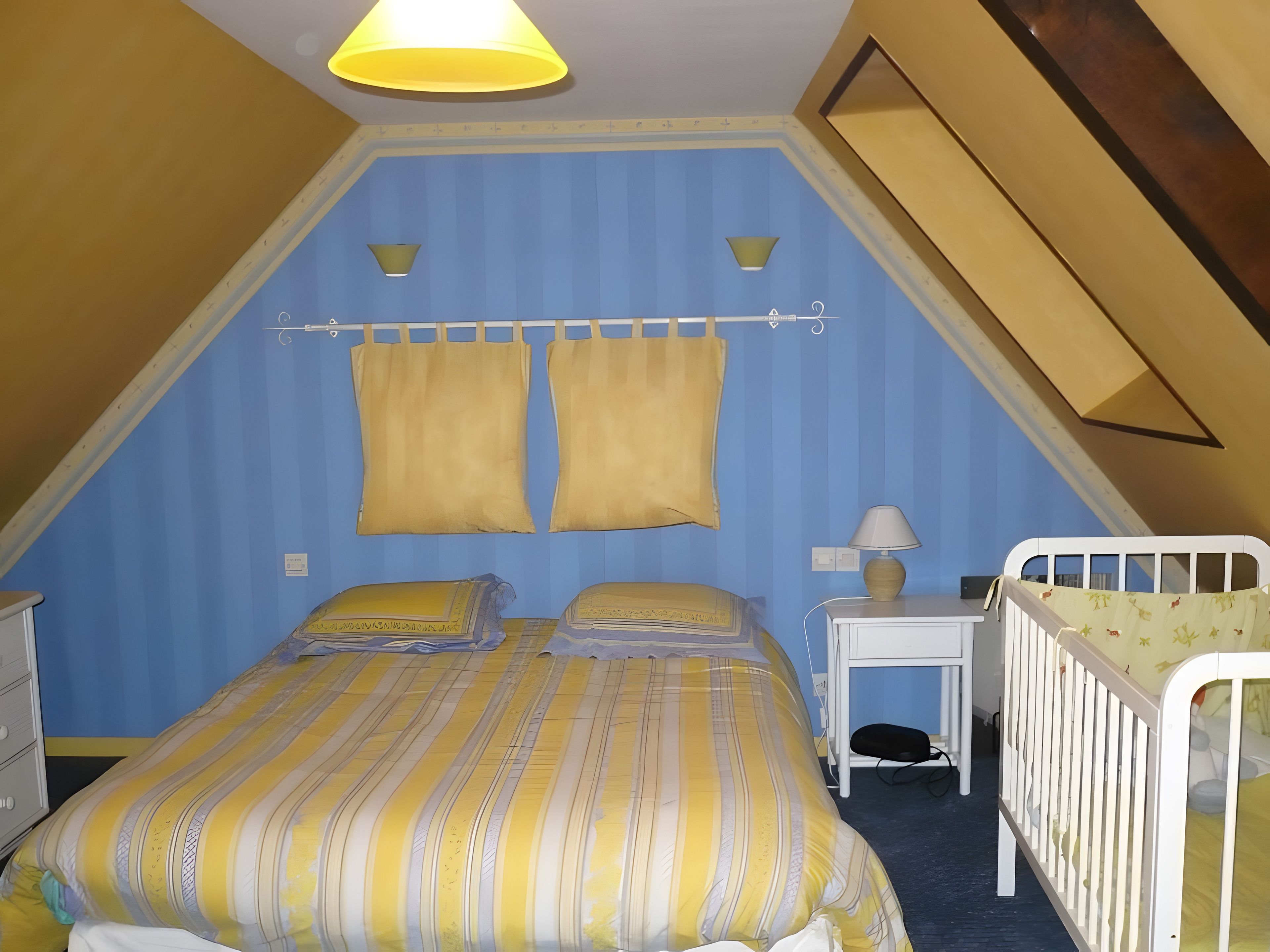 A bedroom with a bed, bedside tables, a lamp, and a crib.