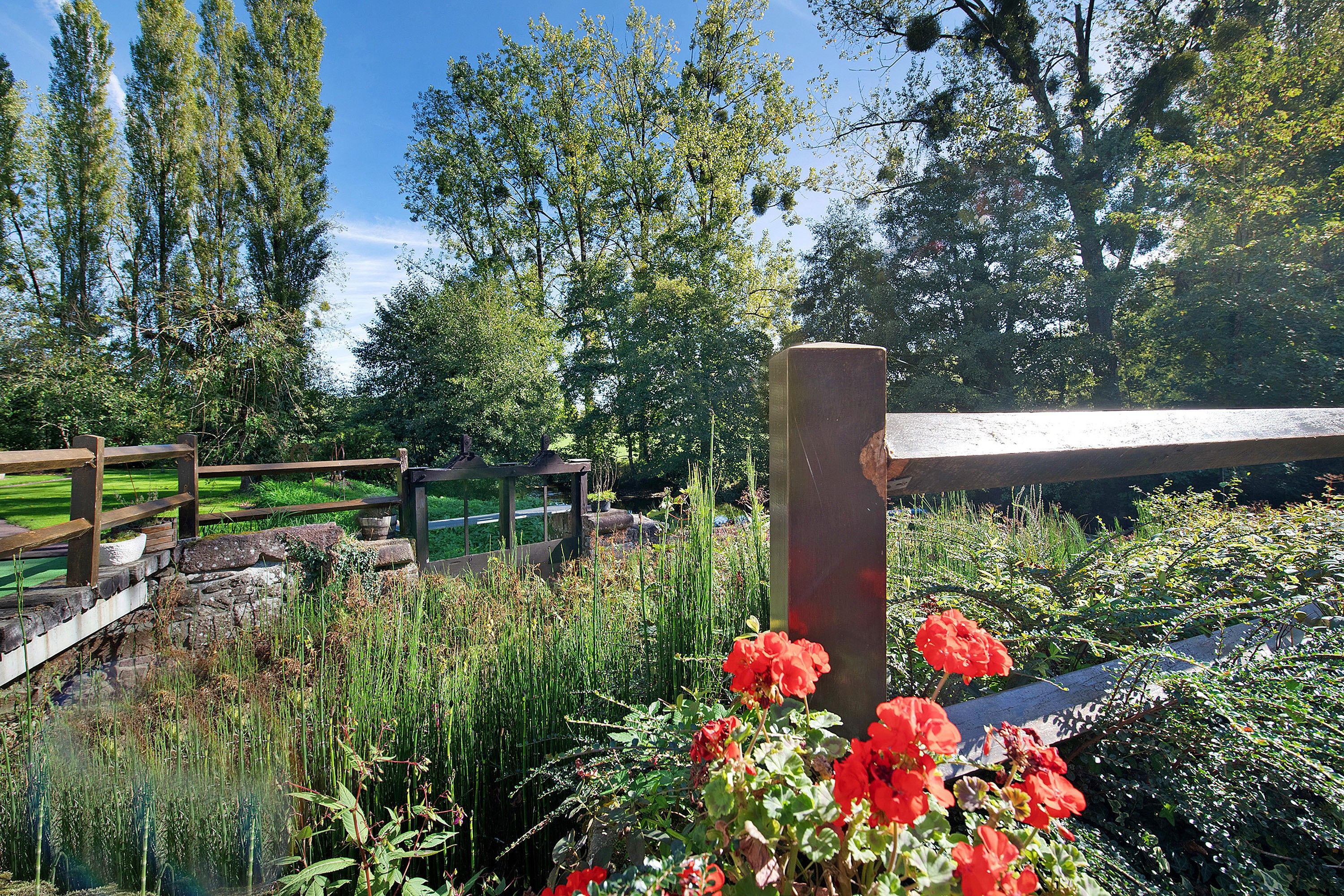 A garden with a wooden fence, a stone wall, and a variety of plants and flowers.