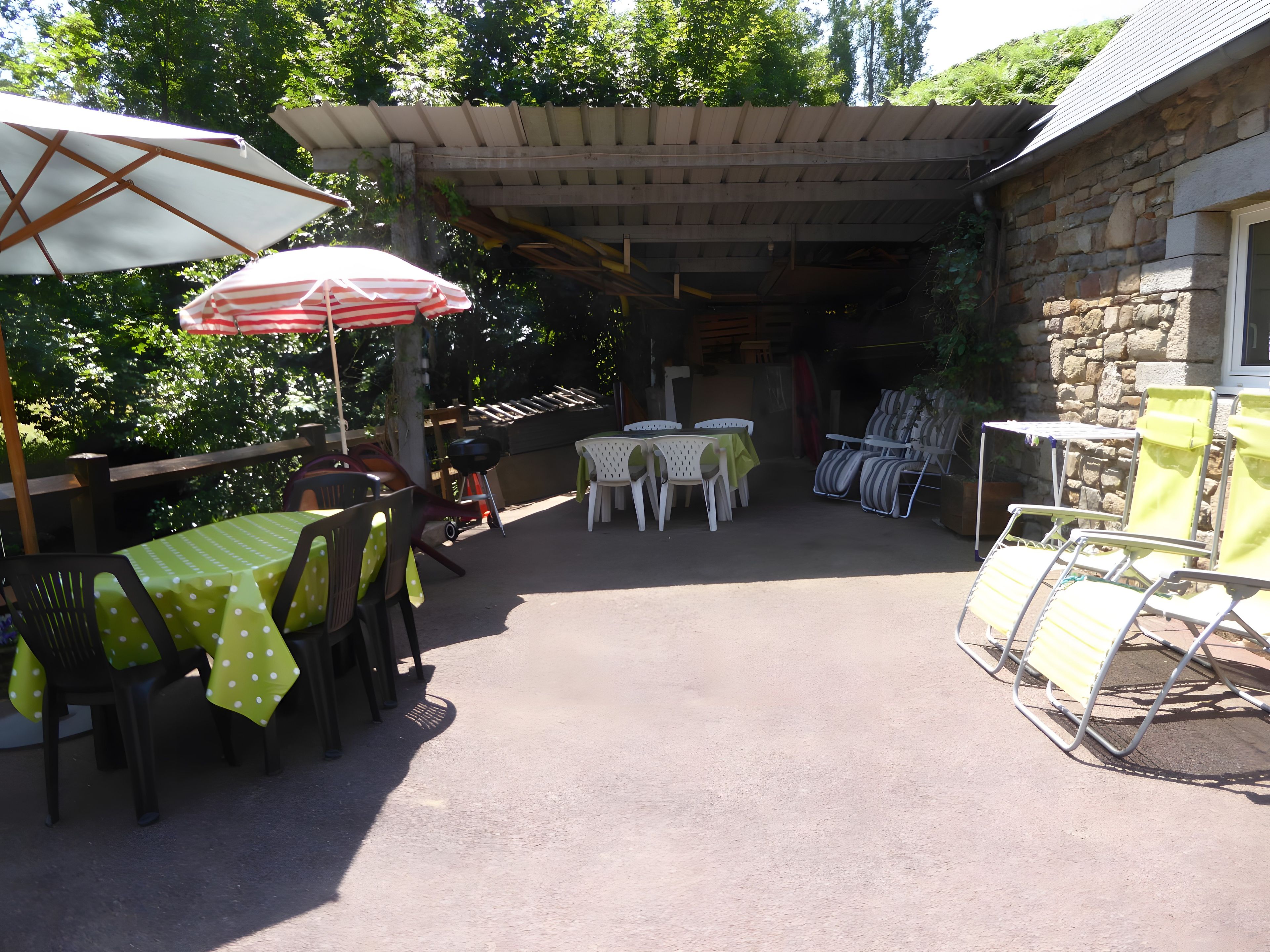An outdoor patio area with tables and chairs, some covered by umbrellas, and a stone building in the background.