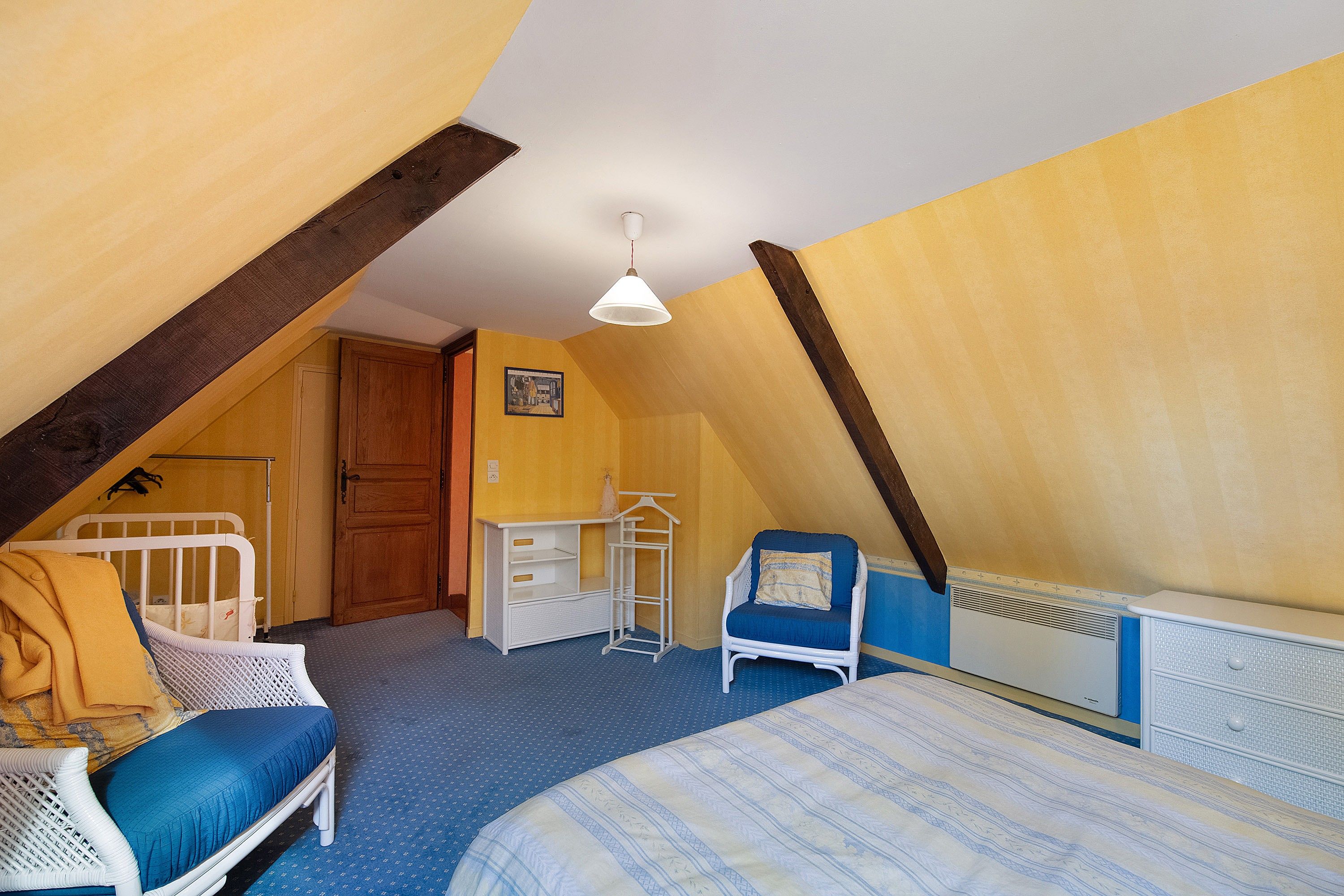 A bedroom with a sloped ceiling, a bed, a chair, a dresser, and a radiator.