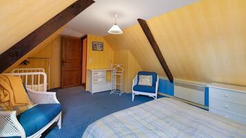 A bedroom with a sloped ceiling, a bed, a chair, a dresser, and a radiator.