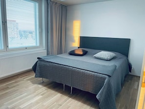Un dormitorio con cama, ventana con persianas, lámpara de noche y radiador.