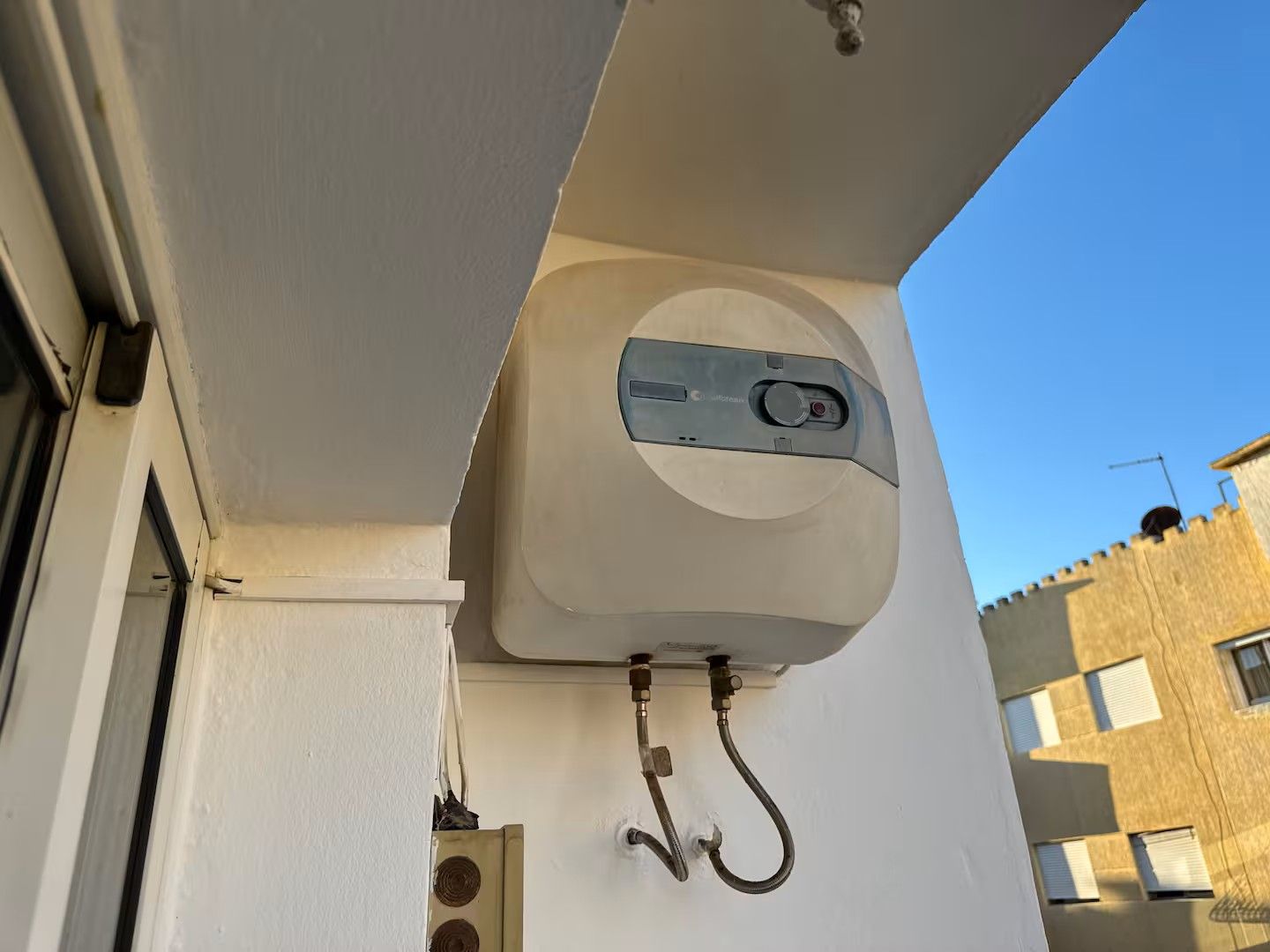 A water tank mounted on a building's exterior wall, connected to a hose.