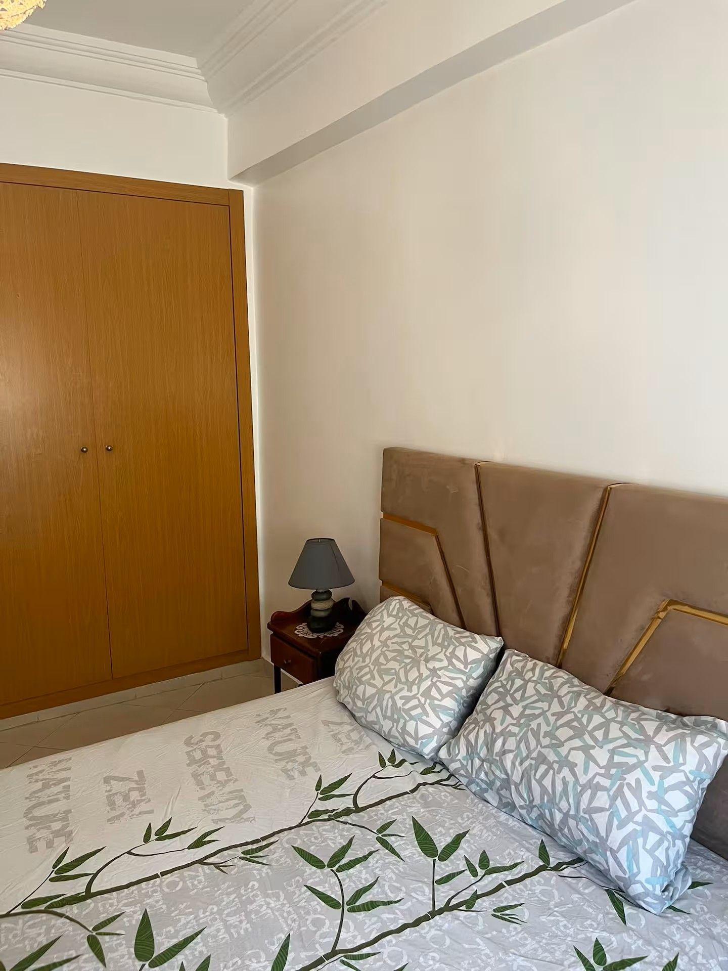 A bedroom with a bed, a nightstand, a lamp, and a wardrobe.