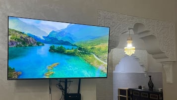 A flat-screen TV mounted on a wall, a decorative wall with intricate patterns, and a small table with a vase and a candle.