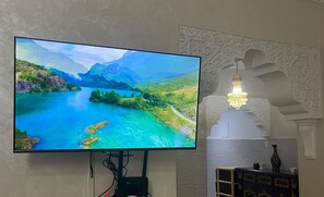 Un televisor de pantalla plana montado en la pared, un diseño de pared decorativo con patrones intrincados y una mesita con un florero y una vela.