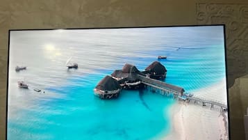 A large screen displaying an aerial view of overwater bungalows connected by a bridge, with boats and calm turquoise waters.