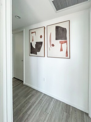 A hallway with two abstract paintings on the wall and a wooden floor. - Alea Miami (Miami)