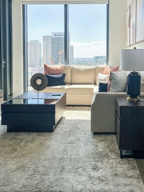 Ein modernes Wohnzimmer mit Sofa, Couchtisch und Lampe, mit Blick auf die Stadt durch große Fenster.
