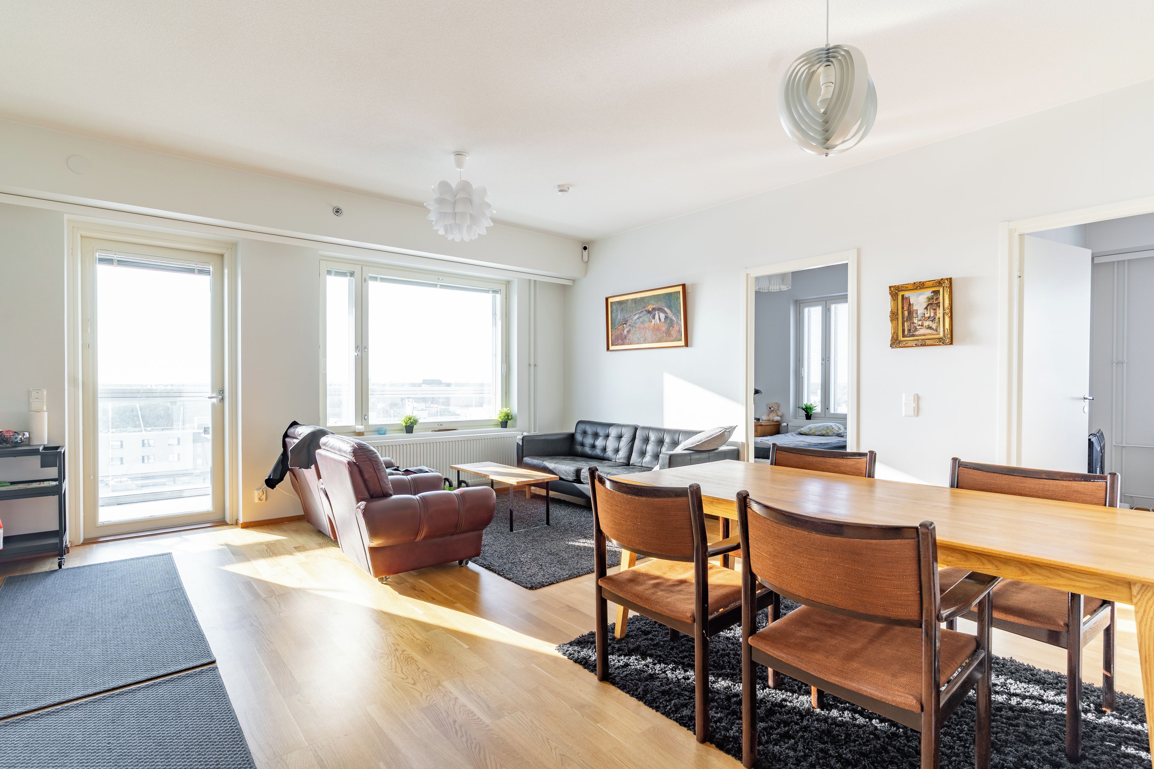 A modern living room with a dining area, large windows, and a city view.