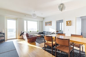 A modern living room with a dining area, large windows, and a city view.