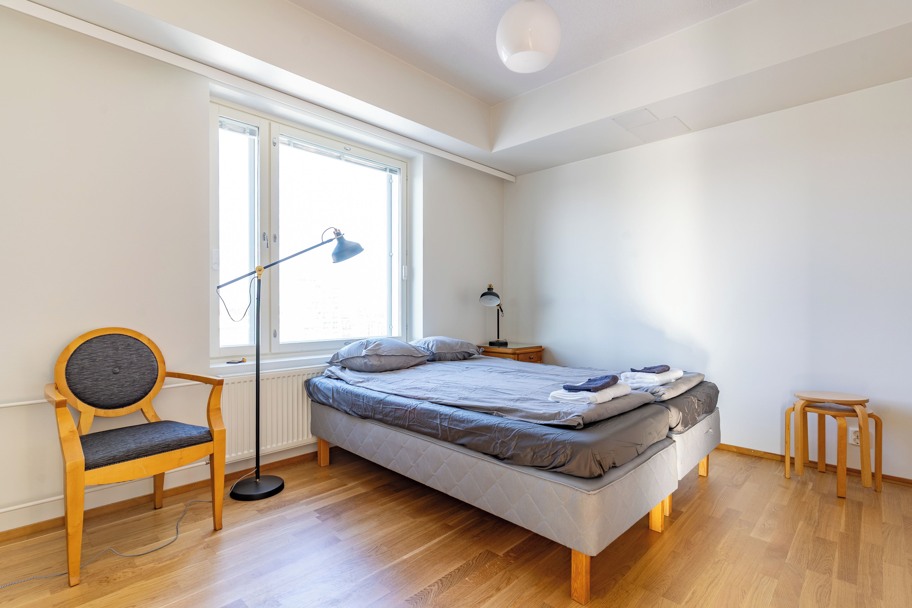 A bedroom with a bed, a chair, a nightstand, a lamp, and a window.