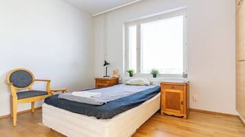 A bedroom with a bed, a chair, a desk, a window, and a bedside table.