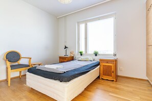 Quarto com cama, cadeira, escrivaninha, janela e mesa de cabeceira.