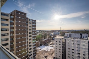 A high-rise building with multiple floors and balconies, overlooking a cityscape with other buildings and a clear sky.