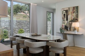 A modern dining area with a round table, six chairs, a stone wall, and a view of greenery outside. - Premium 4-bed villa, superb seaview|Serenity Ocean (Estreito da Calheta)