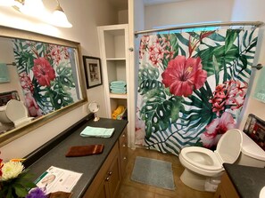 Un baño con inodoro, lavamanos, espejo y cortina de ducha con estampado floral.