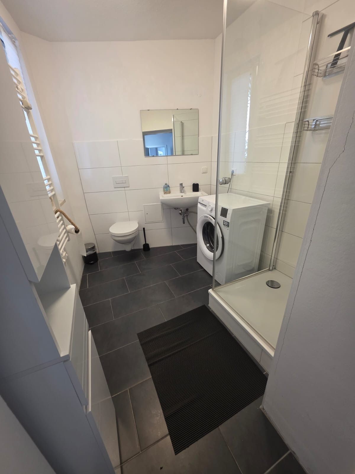 A modern bathroom with a glass shower enclosure, a toilet, a sink, and a washing machine.