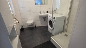 A modern bathroom with a glass shower enclosure, a toilet, a sink, and a washing machine.
