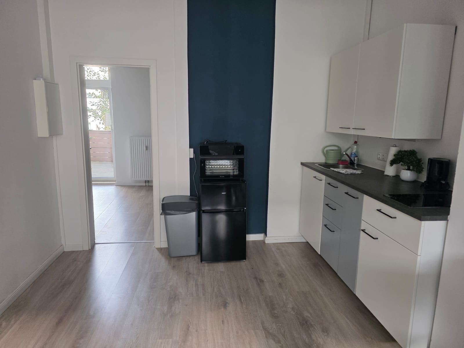 A modern kitchen with white cabinets, a black refrigerator, and a coffee machine.