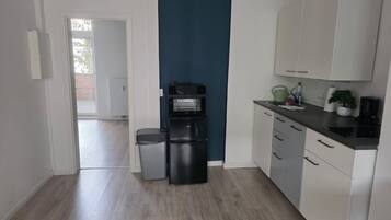 A modern kitchen with white cabinets, a black refrigerator, and a coffee machine.