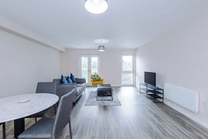 A modern living room with a grey sofa, a round table, and a TV on a stand. - Bright 2BDR Flat in Central Manchester (Manchester)