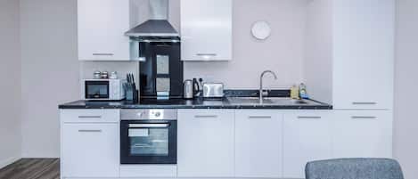 A modern kitchen with white cabinets, a stainless steel range hood, a built-in oven, and a sink.