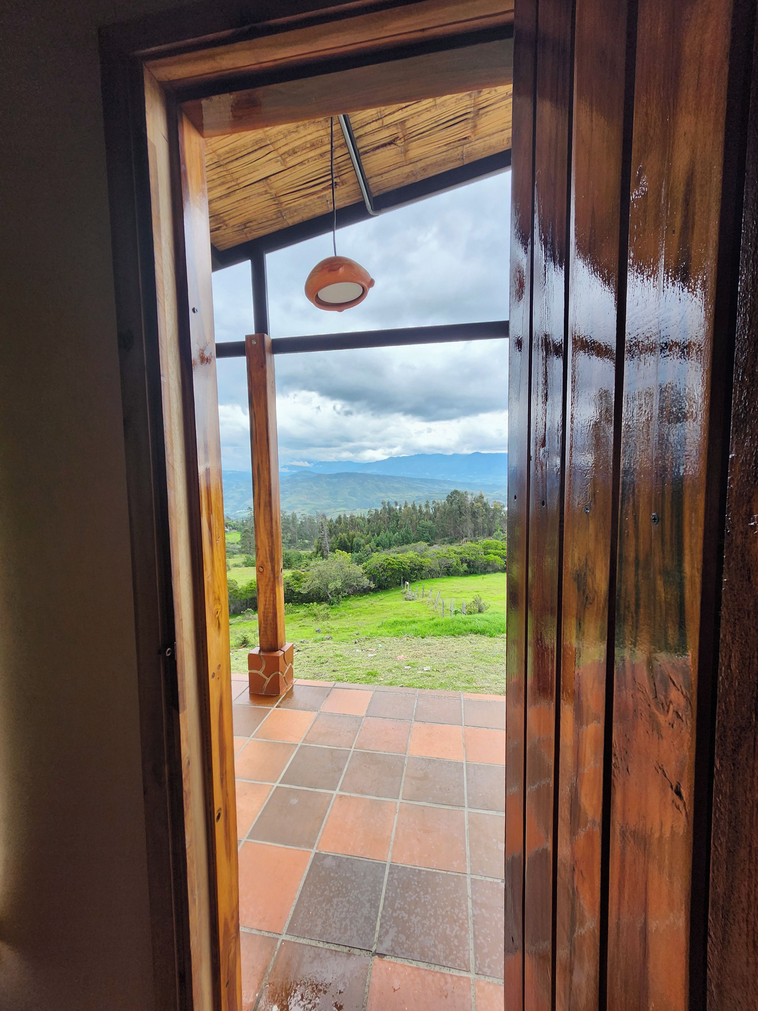 An open wooden door leading to a tiled patio with a hanging light fixture.