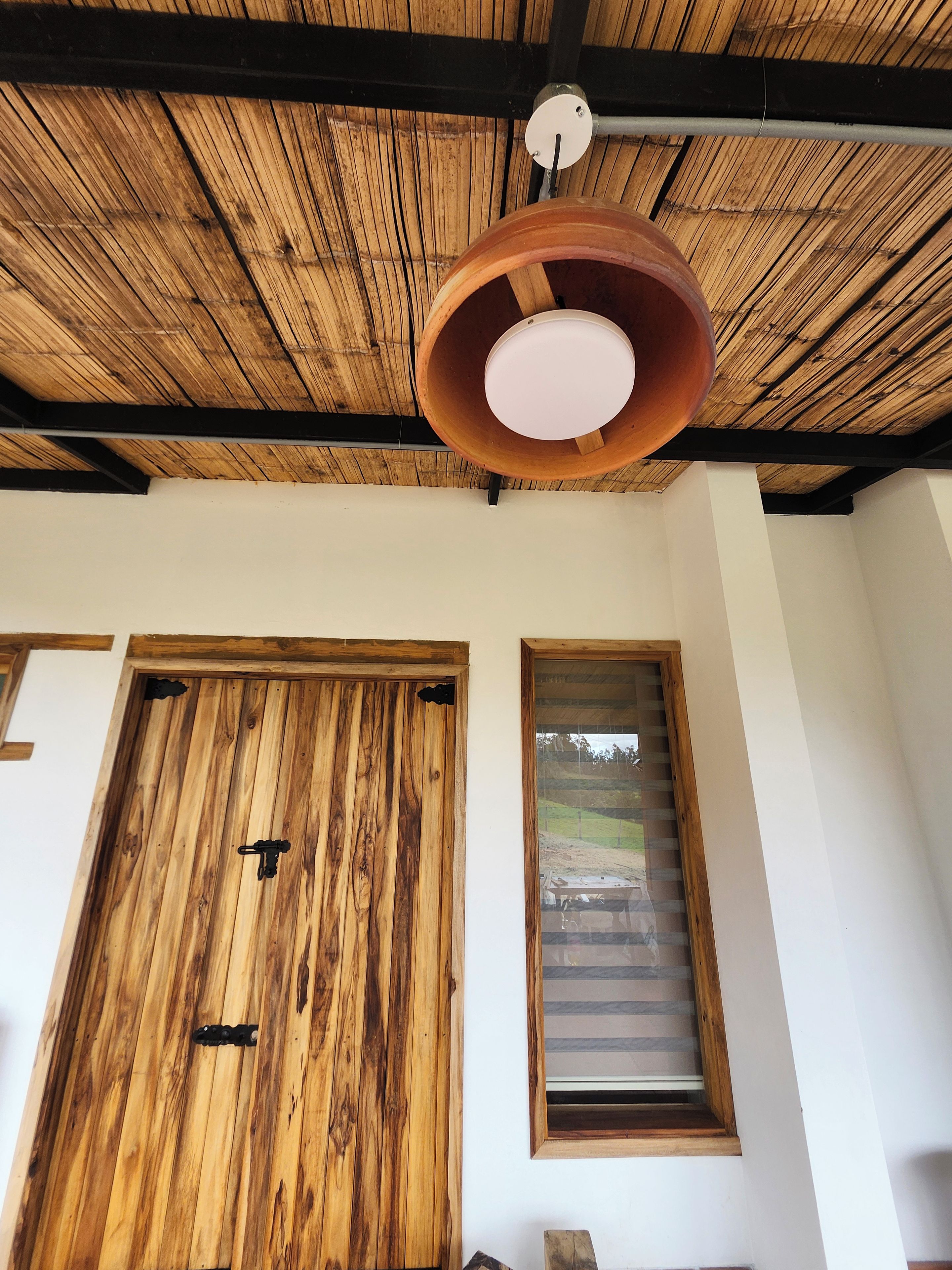 A room with a wooden ceiling, a large wooden door, and a window with blinds.