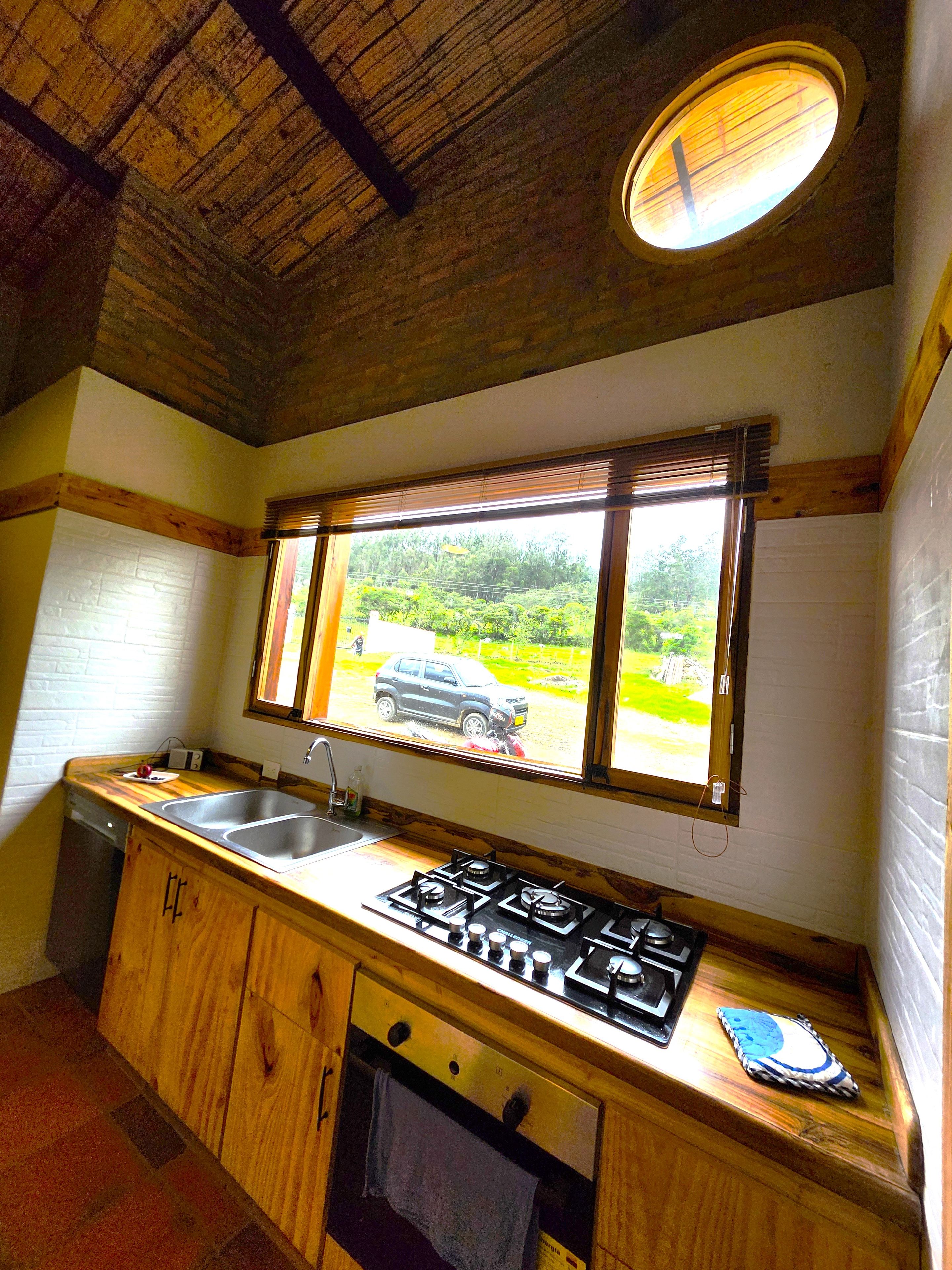 A kitchen with wooden cabinets, a gas stove, a sink, and a window with a view of greenery.