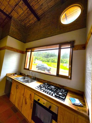 A kitchen with wooden cabinets, a gas stove, a sink, and a window with a view of greenery.