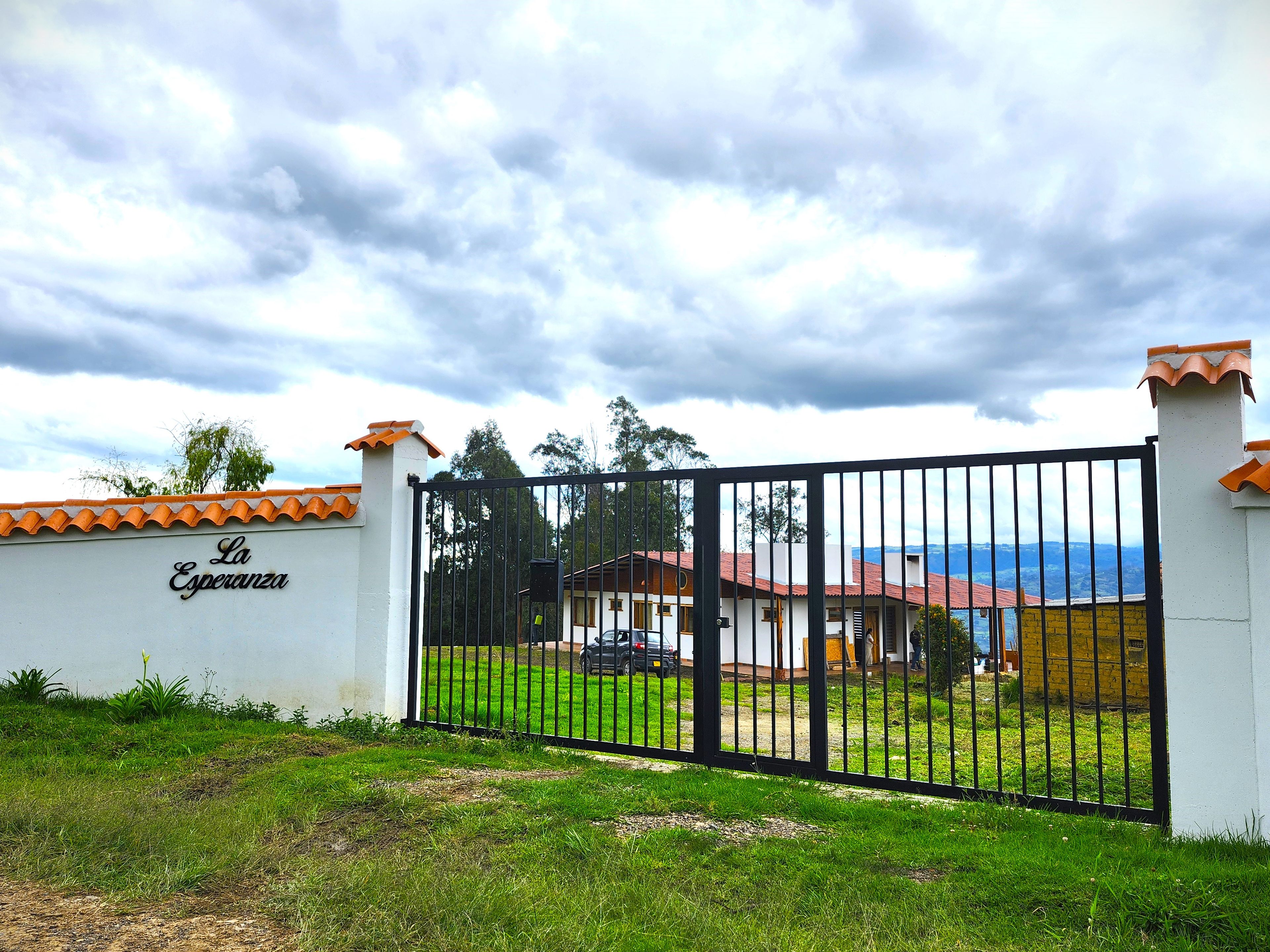 A gated property with a sign reading 'La Esperanza,' a building with a red roof, and a grassy area in front.