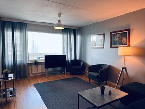 A modern living room with a flat-screen TV, two sofas, a coffee table, and a floor lamp. - Spacious 1BR Near Metro and Major Shopping Center (Espoo)
