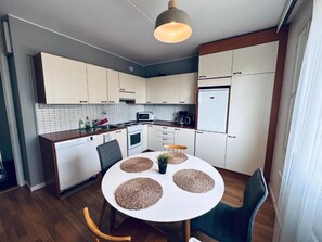 A modern kitchen with white cabinets, a dining table with four woven placemats, and a hanging light fixture. - Spacious 1BR Near Metro and Major Shopping Center (Espoo)