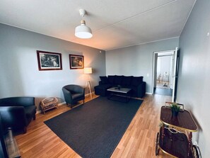 A modern living room with a sofa, armchairs, a coffee table, a lamp, and framed pictures on the wall. - Spacious 1BR Near Metro and Major Shopping Center (Espoo)