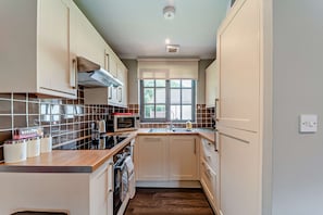 A compact kitchen with a window, a built-in oven, and a stove. - Host and Stay | Lodge 8 (Dailly)