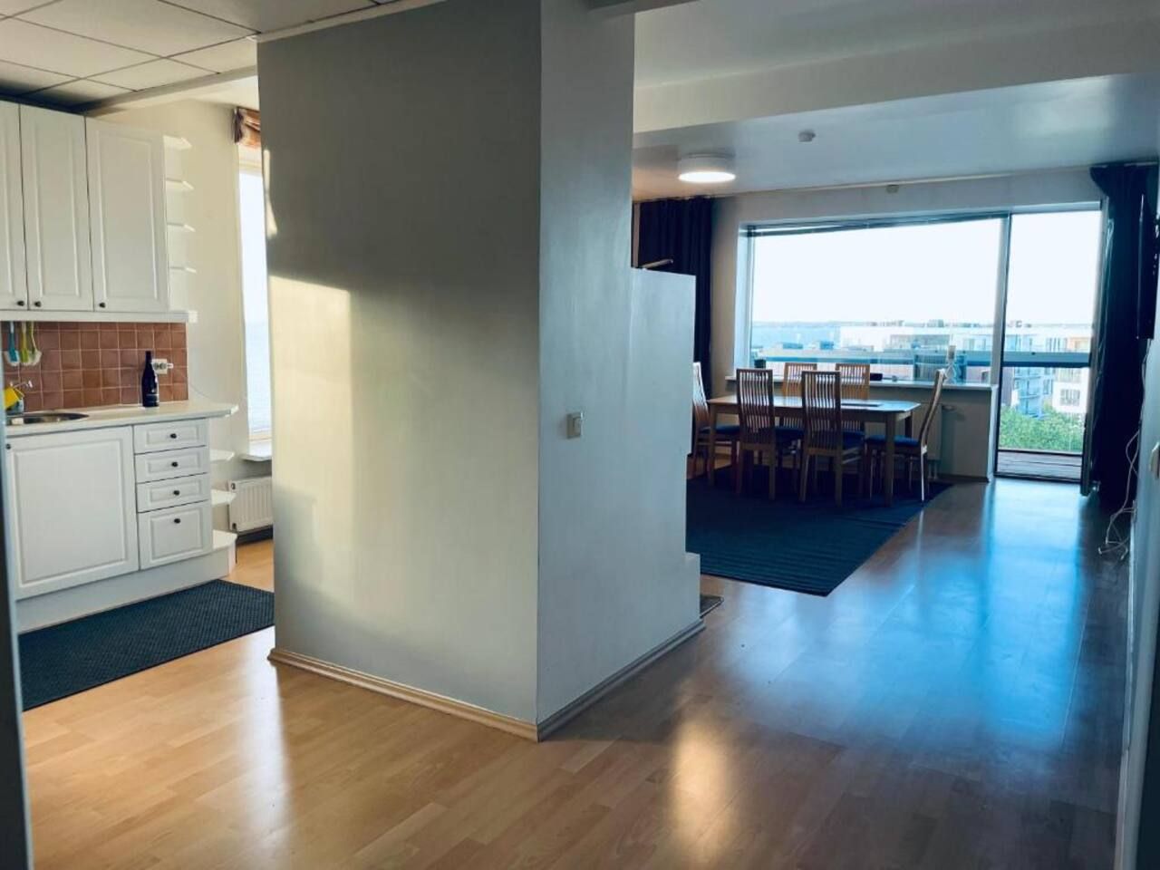 A modern interior with a kitchen, dining area, and a view through a large window.