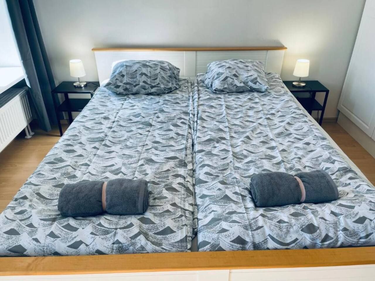 A double bed with patterned bedding, two bedside tables with lamps, and a window with curtains.