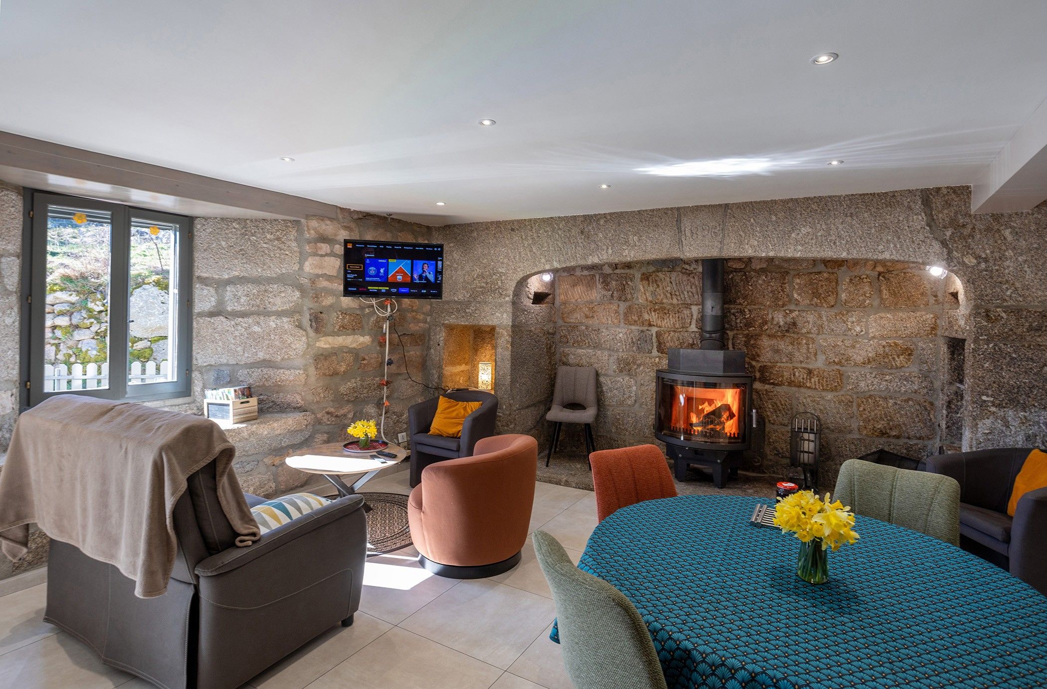 A modern living room with stone walls, a fireplace, comfortable seating, and a flat-screen TV mounted on the wall.