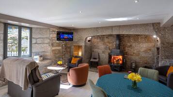 A modern living room with stone walls, a fireplace, comfortable seating, and a flat-screen TV mounted on the wall.
