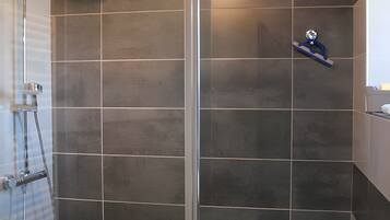 Een moderne badkamer met een glazen douchecabine, donkere betegelde wanden en een wit wastafelmeubel.