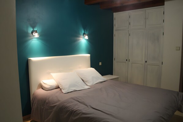 Une chambre à coucher comprenant un lit, deux lampes fixées au mur, une armoire et une table de chevet.