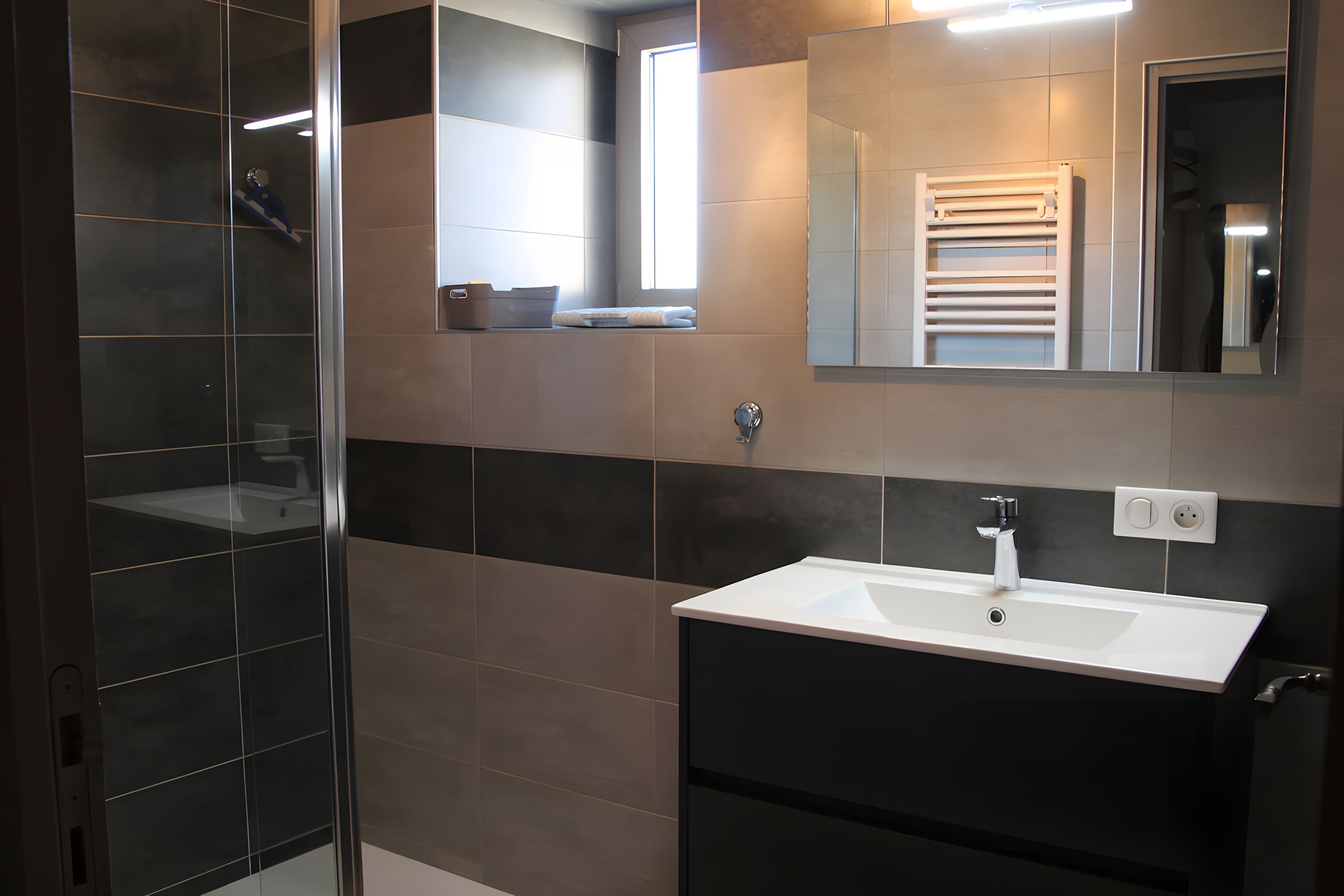 A modern bathroom with a glass shower enclosure, a white sink, and a large mirror.