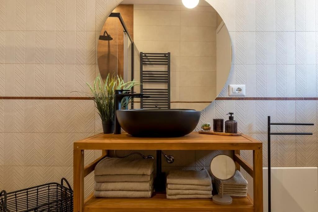 Un bagno con un mobile bagno in legno, uno specchio grande, un lavabo nero, asciugamani, una pianta in vaso e un portascopevoli.