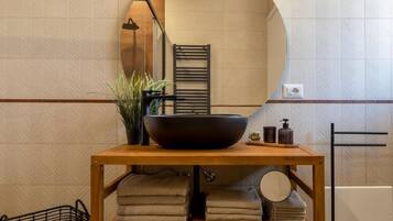 Un bagno con un mobile bagno in legno, uno specchio grande, un lavabo nero, asciugamani, una pianta in vaso e un portascopevoli.