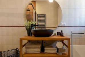 A bathroom with a wooden vanity, a large mirror, a black basin, towels, a potted plant, and a towel rack. - Civico 53 
Your Charming Retreat in the Heart of Sassari (Sassari)